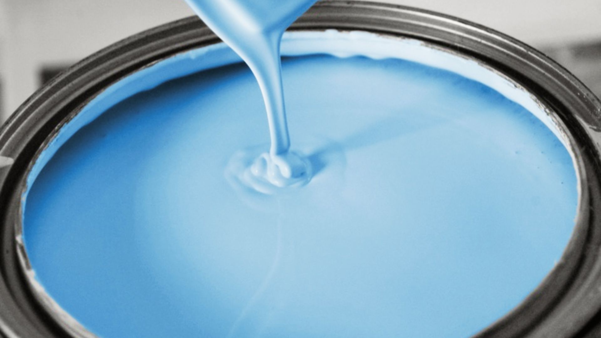 Close-up of bright blue latex paint being poured into an open metal paint can.