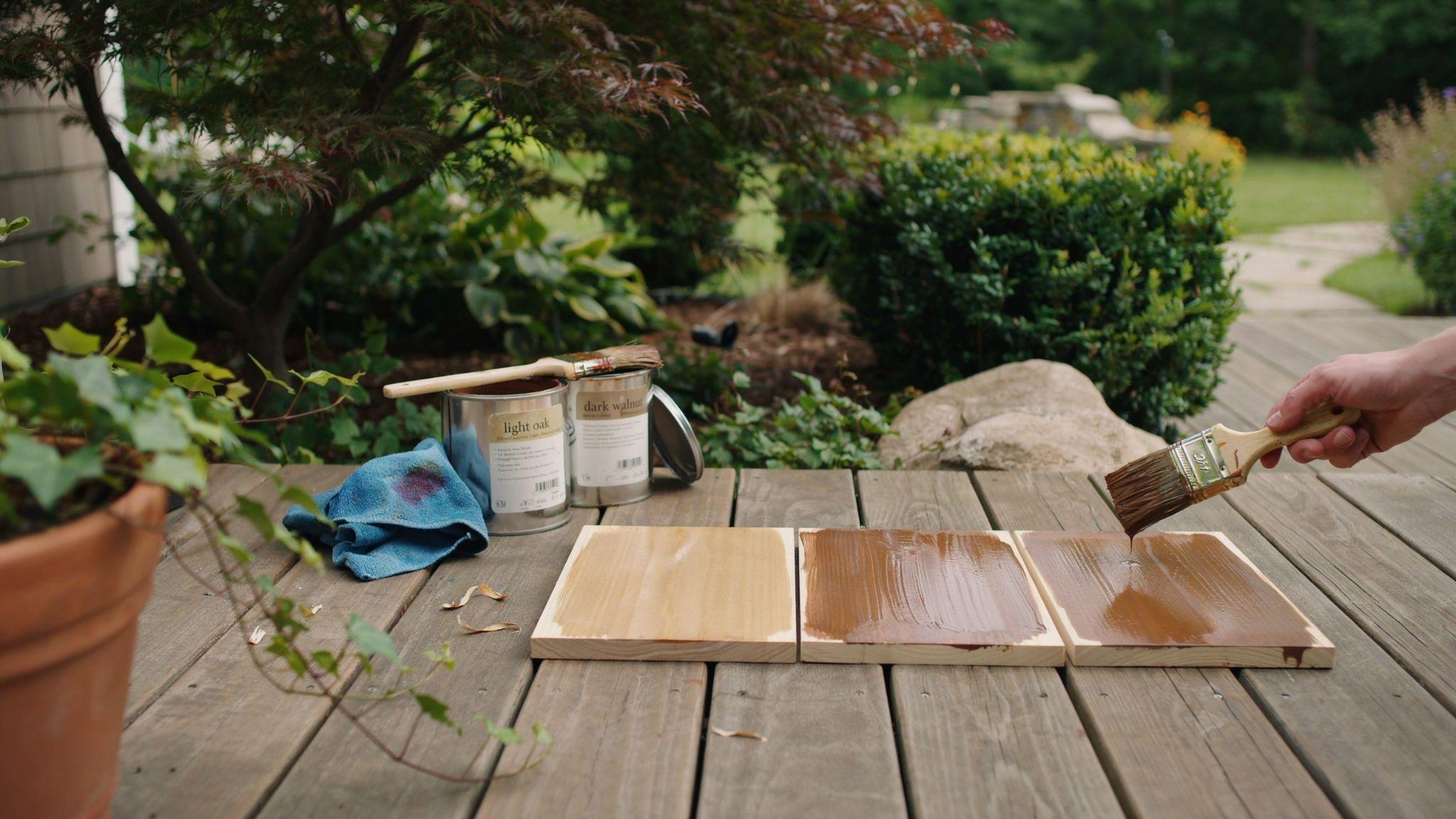 Wood stain sample boards in different shades displayed on a deck as a homeowner compares colors in natural outdoor light.