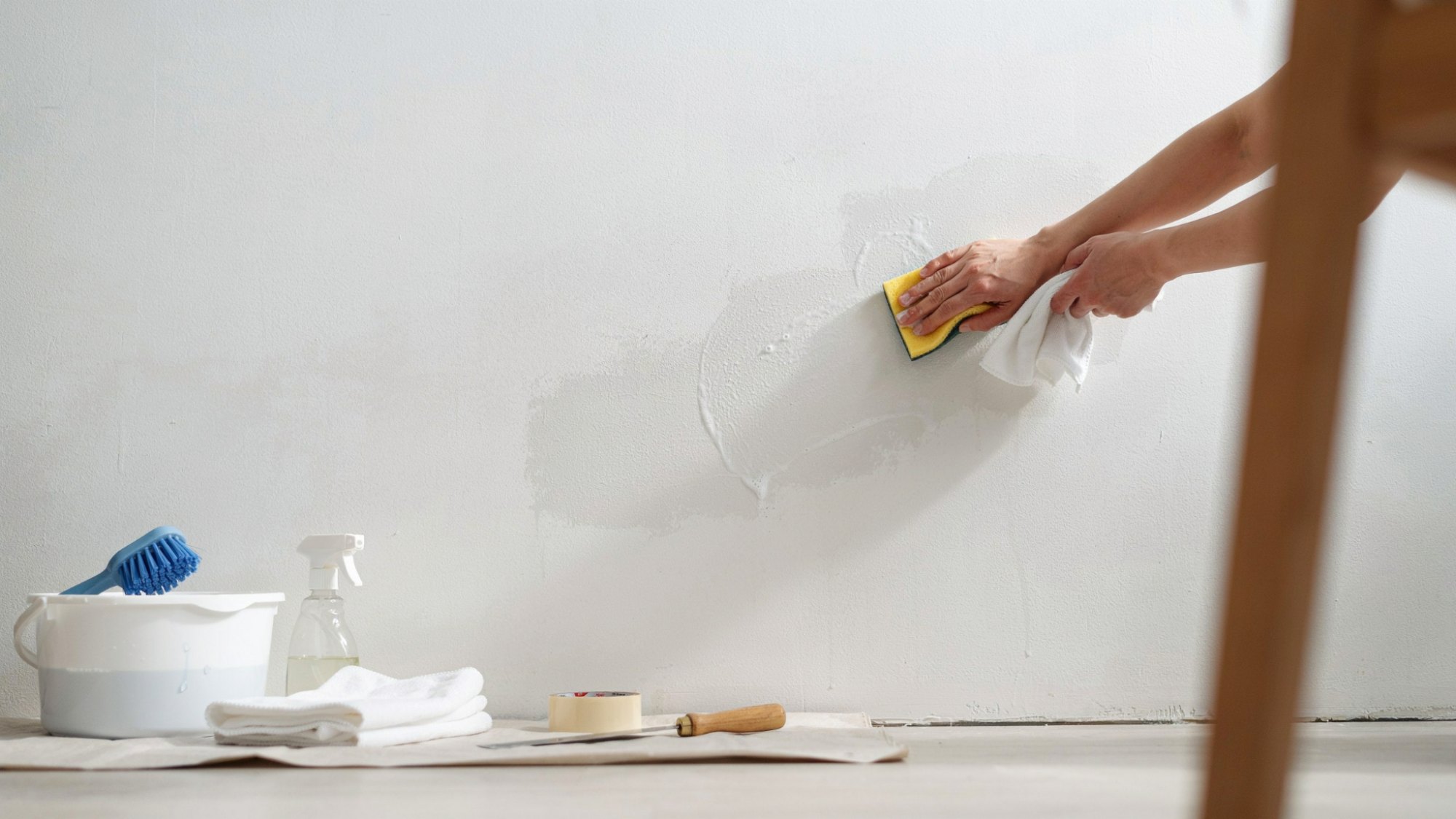 Hands cleaning a painted surface with a sponge to prepare it for painting.