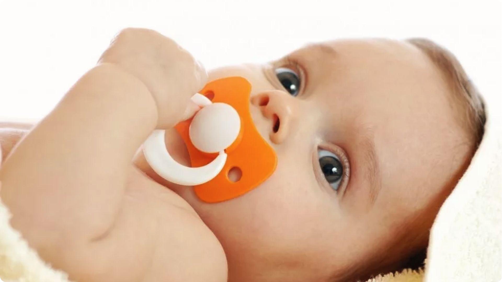 Baby lies with orange pacifier in mouth, illustrating nighttime dependency before starting to wean.