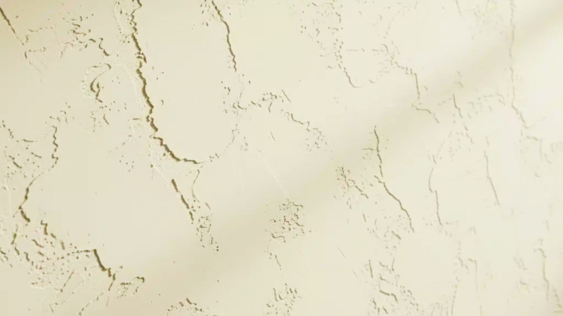 Close-up of beige drywall with Santa Fe texture showing irregular, low-profile ridges and smooth patches.