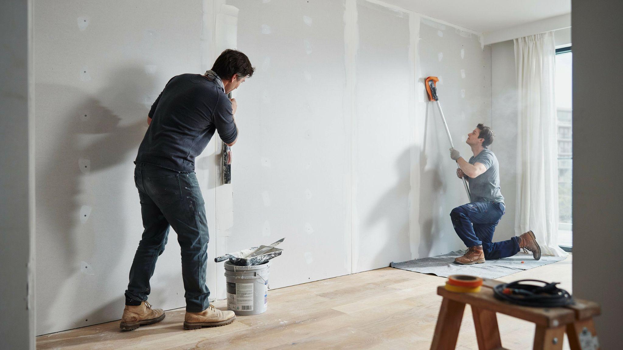 Worker applying and smoothing joint compound over drywall seams during interior wall finishing and renovation.