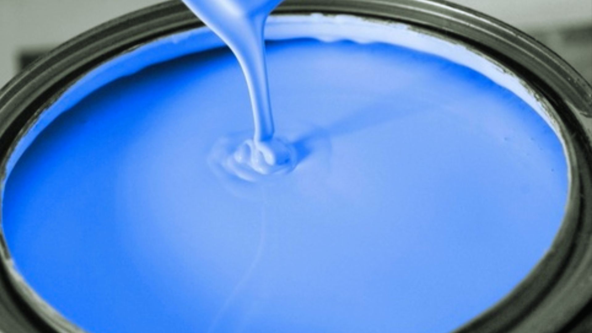 Smooth bright blue paint being poured into an open paint can.