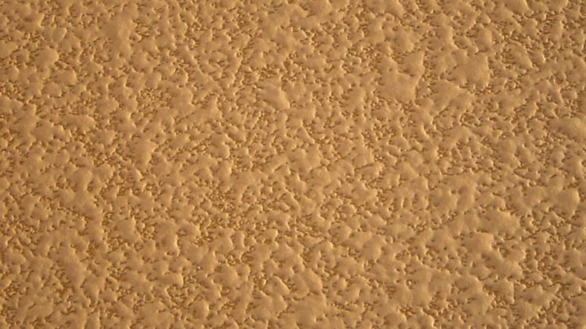 Close-up of a tan wall with heavy orange peel texture, displaying small raised bumps across the entire surface.