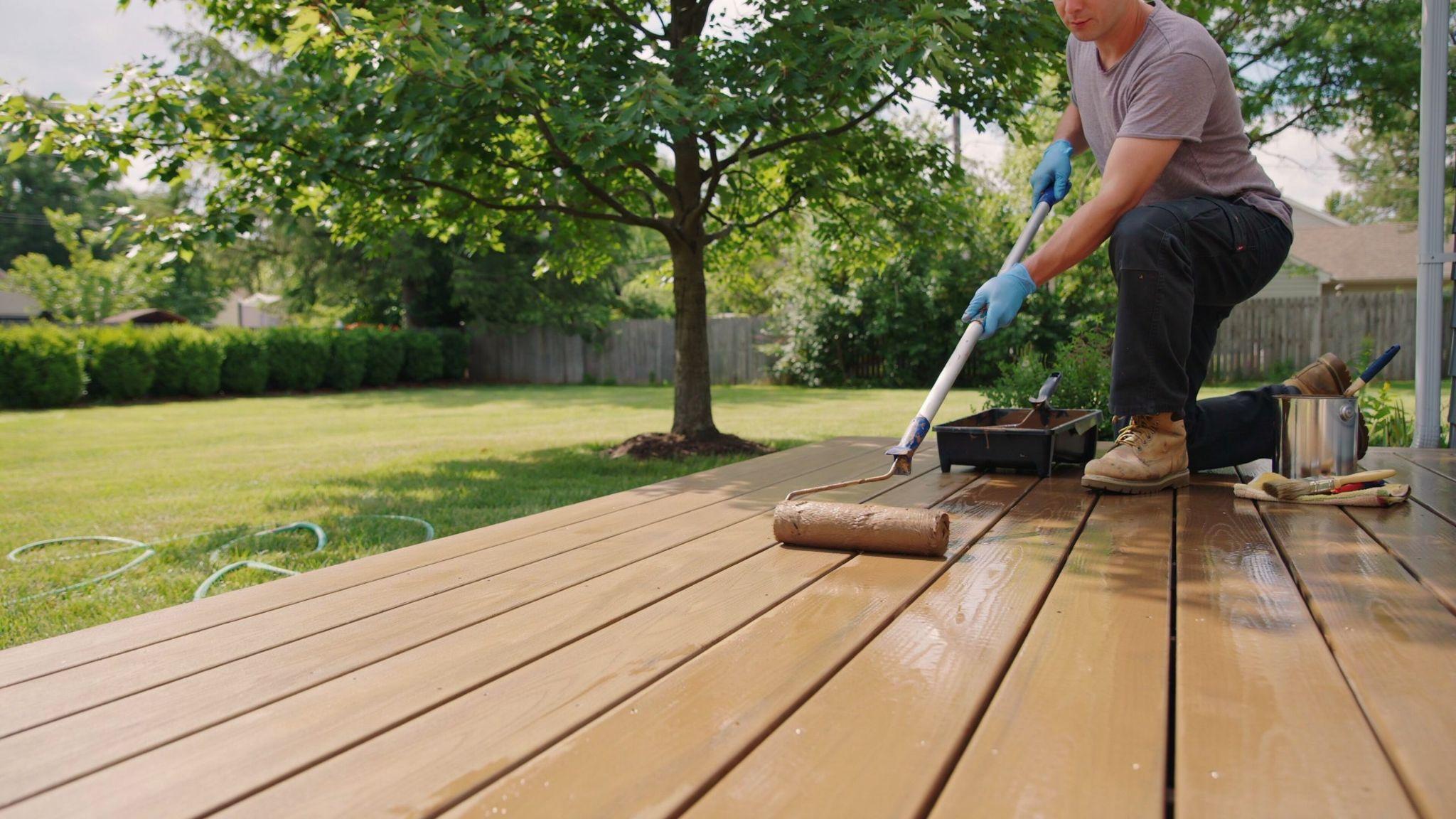 Homeowner using a roller on a wooden deck with smooth, even strokes to achieve a professional-quality stained finish.