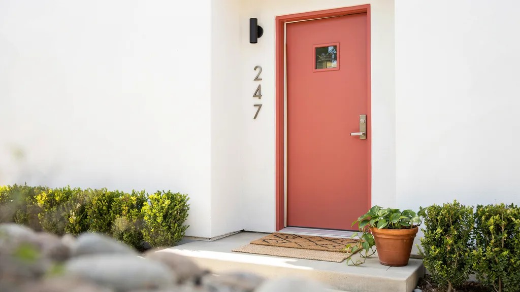 Coral front door on white exterior creating a vibrant and playful entrance, adding energy and a perfect modern touch to the home.